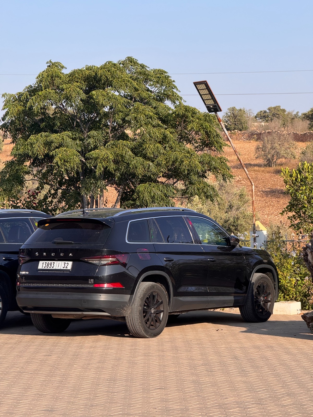 Kodiaq — Rear Profile Rear three-quarter view of a black Škoda Kodiaq parked under trees in the Moroccan countryside